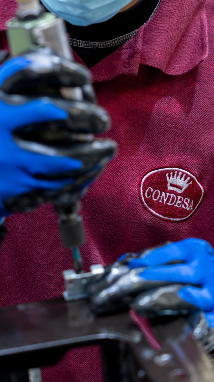 Detalle de manos con guantes azules y uniforme con logo bordado durante el trabajo en la línea de producción